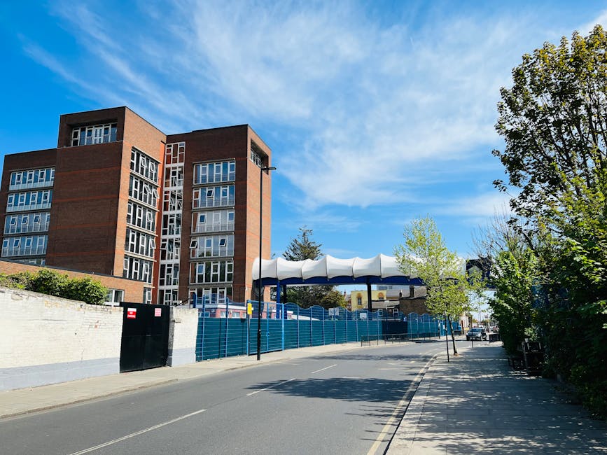 There is no image provided of flowers or floral arrangements; the visible scene shows a street with a large brick residential building, a blue construction fence, and a white-and-blue canopy structure