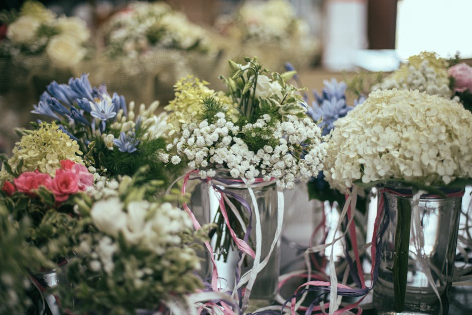 A close-up of several glass vases filled with fresh flower arrangements placed on a table. The arrangements include clusters of white hydrangeas with large, rounded blooms, delicate white baby's breat